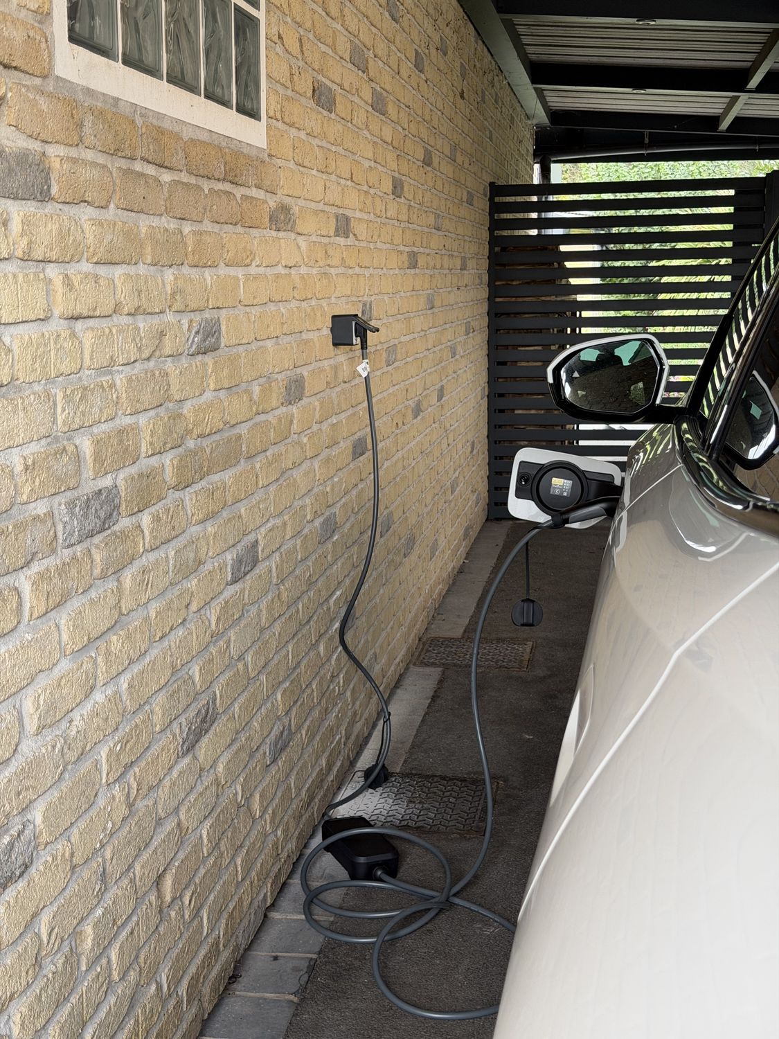 Véhicule électrique en charge dans un carport sur une prise murale dédiée